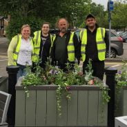 Four people standing behind a flower planter.