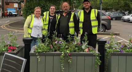 Four people standing behind a flower planter.