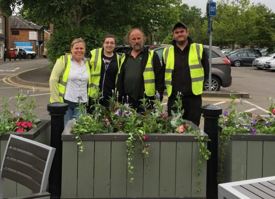 Four people standing behind a flower planter.