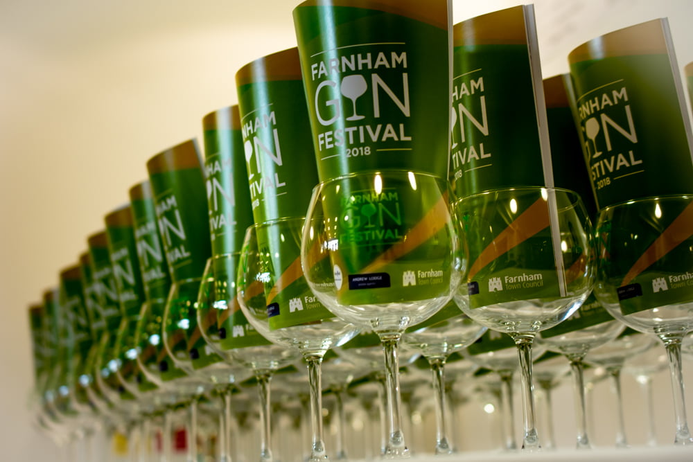 Row of stemmed glasses with a green Gin Festival programme inserted in each