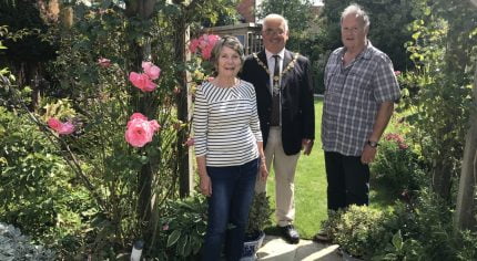 Female, Mayor and male stand under an archway in a pretty garden.