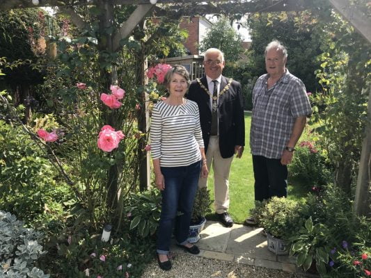 Female, Mayor and male stand under an archway in a pretty garden.