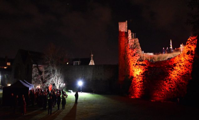 Group of people standing near a wall that is lit up with red light.