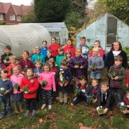 Children standing in front of an allotment holding potted plants.