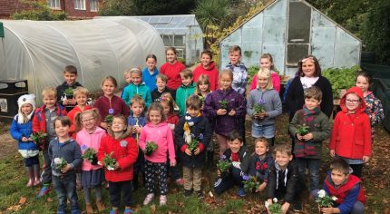 Children standing in front of an allotment holding potted plants.