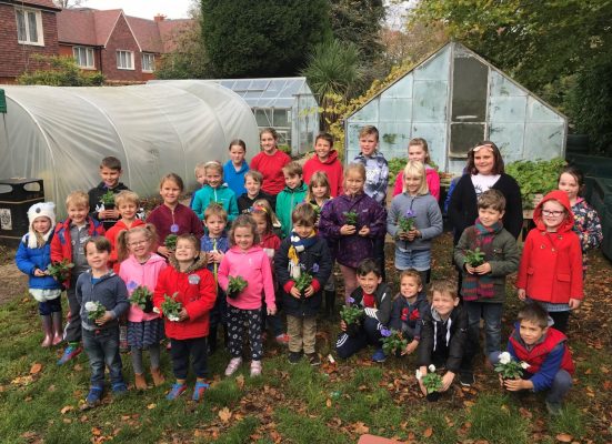 Children standing in front of an allotment holding potted plants.