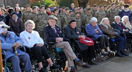 Older people in wheelchairs and soldiers standing behind.