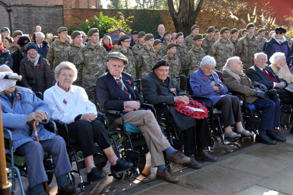 Older people in wheelchairs and soldiers standing behind.