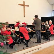 Brass band sitting on a stage wearing Christmas hats.