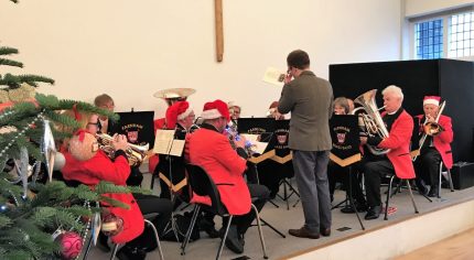 Brass band sitting on a stage wearing Christmas hats.