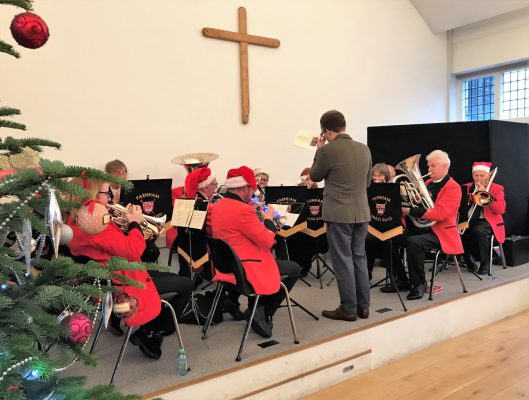 Brass band sitting on a stage wearing Christmas hats.