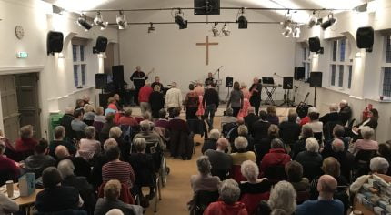 Older people watching a band perform inside a church hall