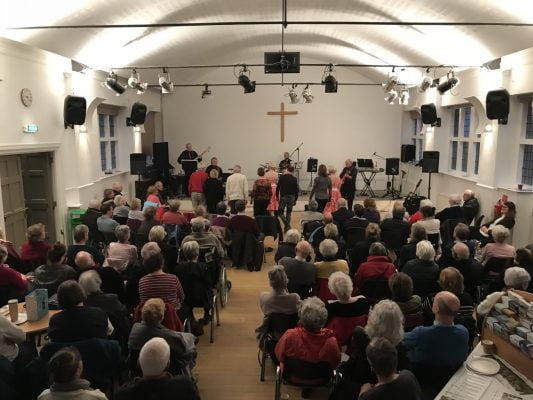 Older people watching a band perform inside a church hall