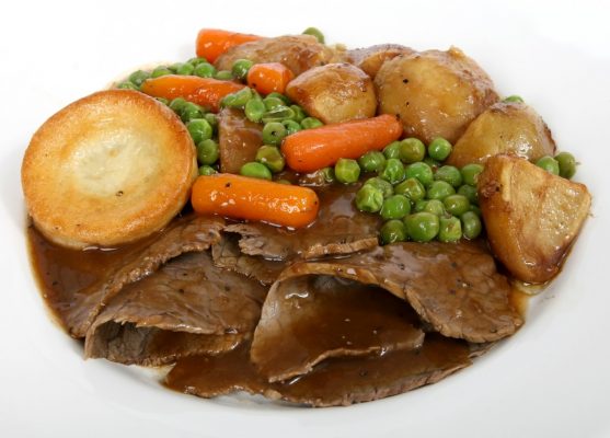 Plate of roast beef, Yorkshire pudding, roast potatoes, peas, carrots and gravy.