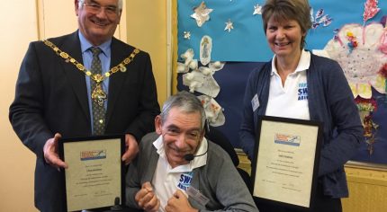 Man in wheelchair with the Mayor and a female holding certificates.