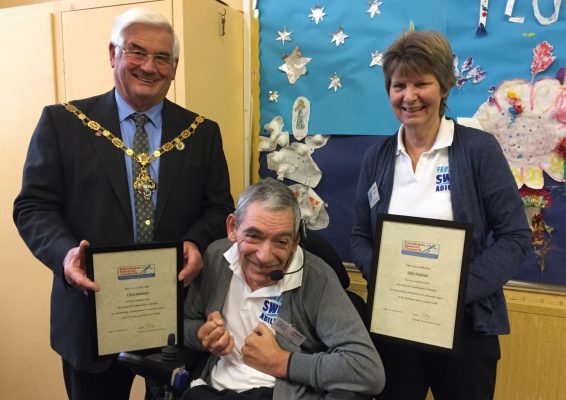 Man in wheelchair with the Mayor and a female holding certificates.