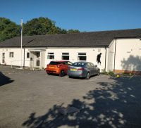 Outside of white single storey building with two cars parked in front.