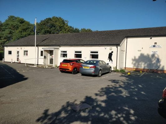 Outside of white single storey building with two cars parked in front.