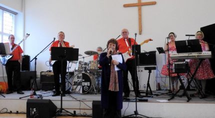 Female on microphone. Band behind her on a stage.