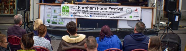 People sitting in front of a stage watching a Food Festival demonstration.