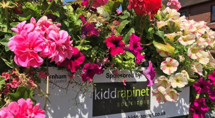 Close up of pink, purple and white flowers in a trough with a plaque on the container showing a sponsor's name.