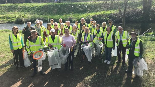Group of people in high viz jackets holding sacks and litter picks