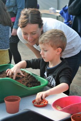 Boy plants pea seeds in a plant pot watched by smiling female