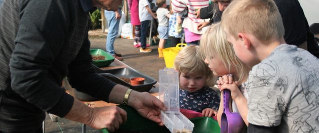 Man shows children a container of seeds.