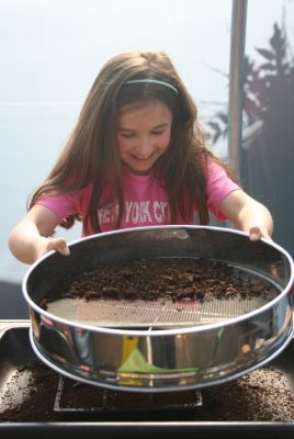 Young girl sieves soil onto a plastic plant pot