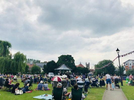 People sitting in a park watching live music in a bandstand.