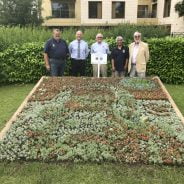 Five people standing behind a flower bed