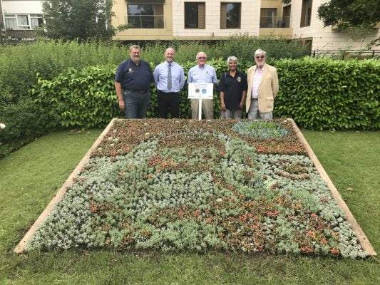 Five people standing behind a flower bed