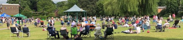 People sitting in a park watching live music in a bandstand.