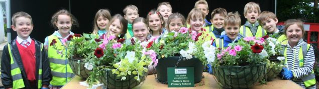 Group of children standing behind a table full of hanging baskets.