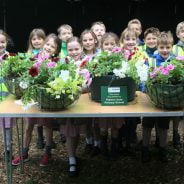 Group of children standing behind a table full of hanging baskets.