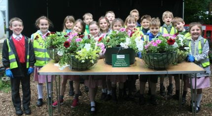 Group of children standing behind a table full of hanging baskets.