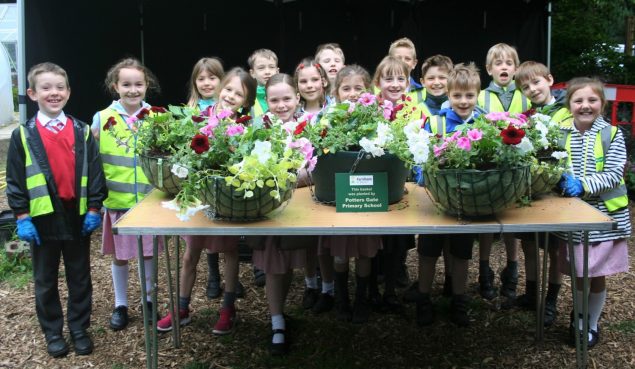 Group of children standing behind a table full of hanging baskets.