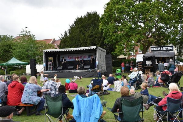 Crowd of people in a park watching live music on a stage.