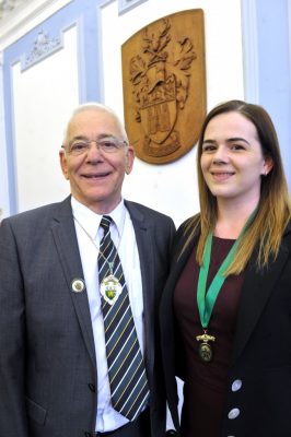 Smiling man in suit wearing a deputy Mayor's badge standing next to female.