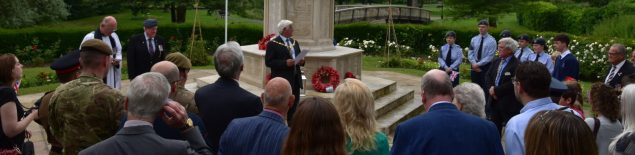 Group of people standing in semi circle facing war memorial