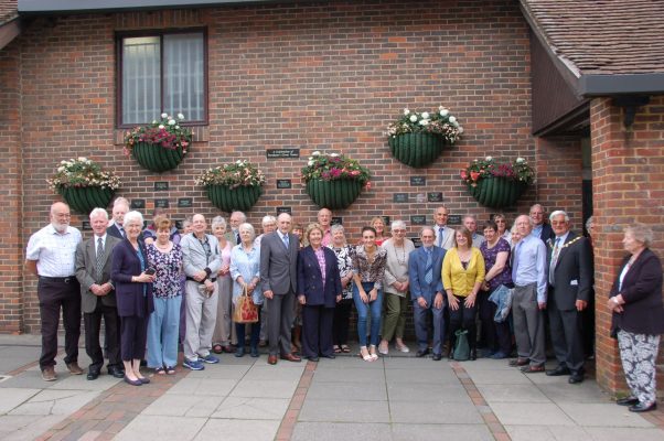 Large group of people standing in front of a wall featuring commemorative plaques.