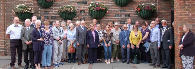 Large group of people standing in front of a wall featuring commemorative plaques.