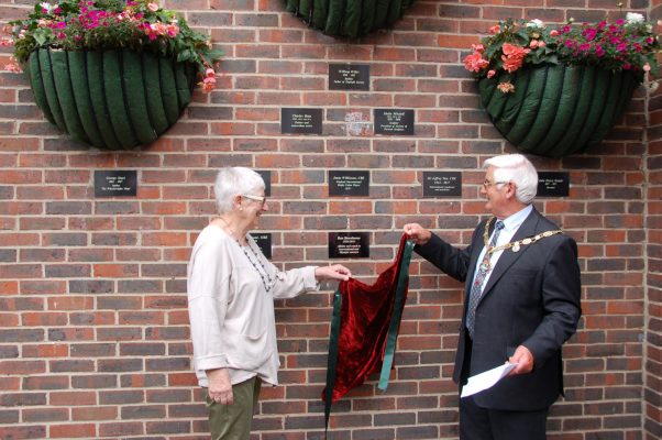 Mayor and female remove a drape to unveil a plaque on a wall.