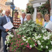 Group of people standing behind a hop cart filled with flowers.