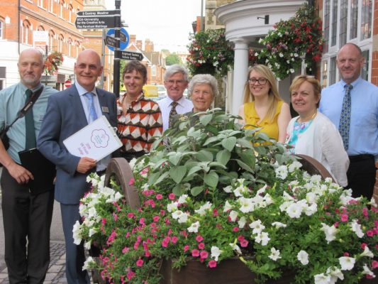 Group of people standing behind a hop cart filled with flowers.