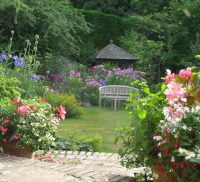 Large garden, flower beds to left and right, summer house and bench in background and patio in foreground.