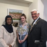 Two females and man stand in front of a painting of poppies.