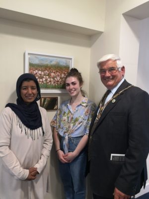 Two females and man stand in front of a painting of poppies.