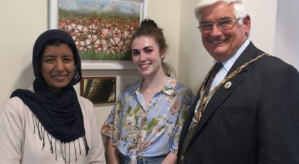 Two females and man stand in front of a painting of poppies.