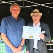 Two men in a marquee. Man on right presents a certificate.